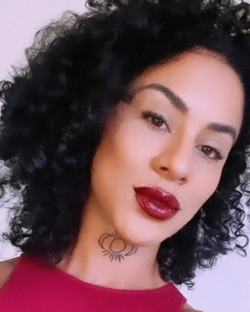 Retrato de Lorena Modesto, de cabelo cacheado, batom vermelho e blusa vermelha